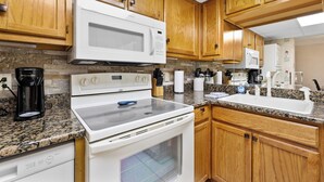 A kitchen with wooden cabinets, a white microwave, a stove, and a sink. - 2 BR Condo on the River! Walk to the Island (Pigeon Forge)
