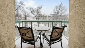 A balcony with two chairs and a table, overlooking a snowy landscape with buildings in the background. - 2 BR Condo on the River! Walk to the Island (Pigeon Forge)