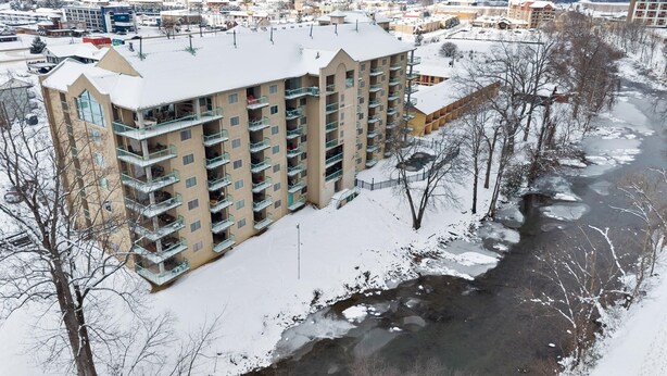 A multi-story hotel with balconies, a river in the foreground, and a mountainous backdrop. - 2 BR Condo on the River! Walk to the Island (Pigeon Forge)