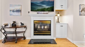 A fireplace with a mantel, a mounted television above it, and a small table with decorative items beside it. - 2 BR Condo on the River! Walk to the Island (Pigeon Forge)