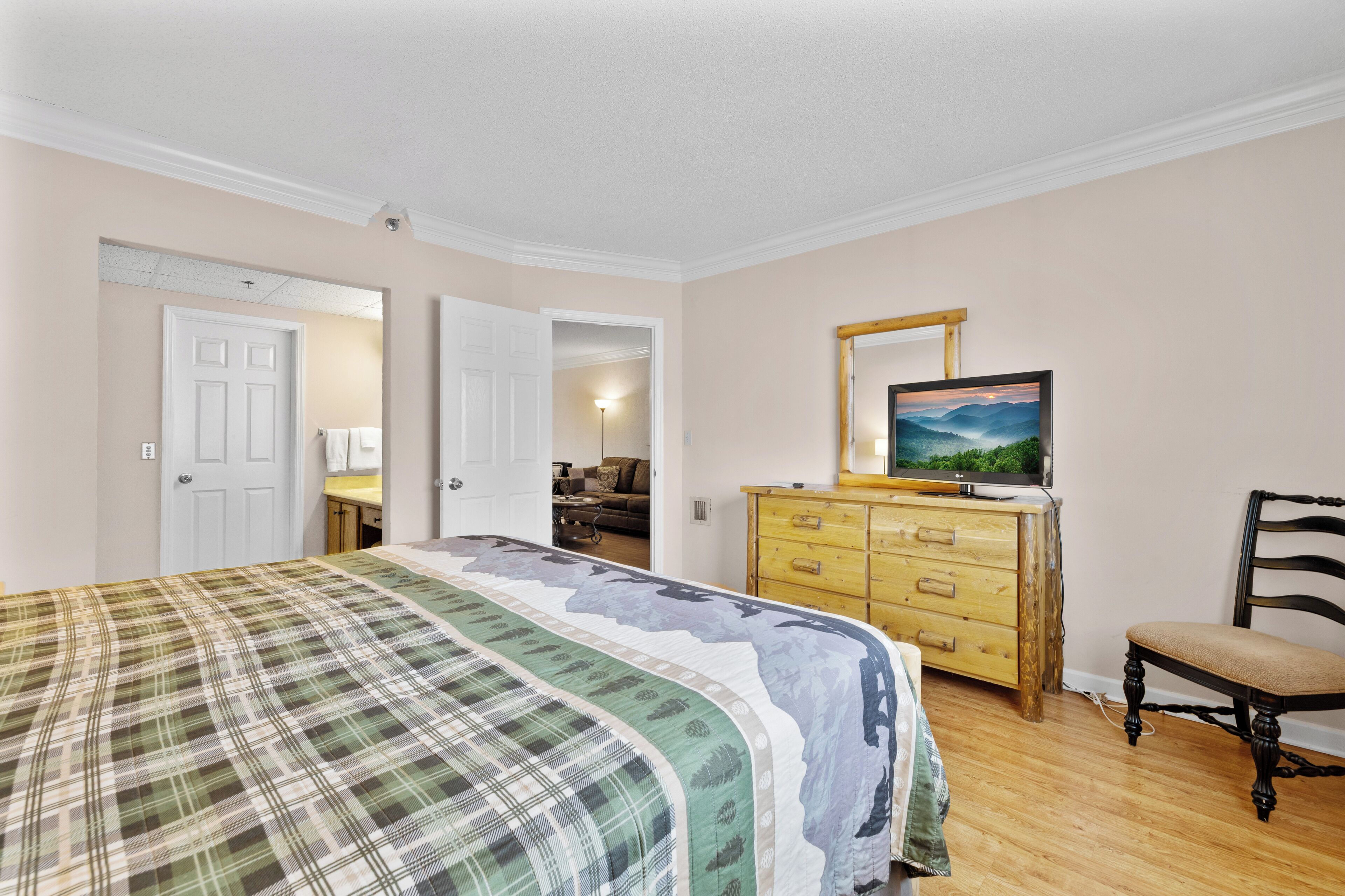 A bedroom with a bed, dresser, chair, and a painting on the wall.