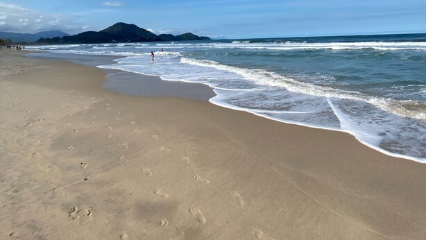 A beach with footprints in the sand and waves approaching the shore.
