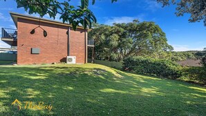 A brick building with a small attached garage, a lawn, and a large tree. - Amaroo Cres No 20 Fingal Bay Holiday Home (Fingal Bay)