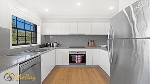 A modern kitchen with white cabinets, stainless steel appliances, and a window with a view of greenery.
