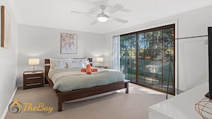 A bedroom with a bed, two bedside tables, a ceiling fan, a large window, and a framed artwork on the wall.