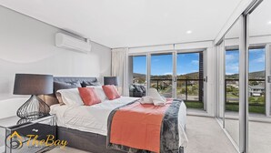 Un dormitorio moderno con una cama grande, una mesita de noche con lámpara y vistas a un paisaje verde a través de ventanales de pared a techo.