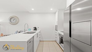 Una cocina moderna con armarios blancos, un refrigerador de acero inoxidable, horno empotrado y un reloj en la pared.