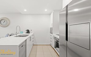 Una cucina moderna con mobili bianchi, un frigorifero in acciaio inossidabile, forno integrato e un orologio a parete.