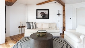 A living room with a white sofa, a round coffee table with a glass top, a framed bull picture on the wall, and a tall floor lamp. - HISTORIC DOWNTOWN LOFT (Sevierville)