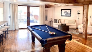 A pool table in a room with wooden beams, a sofa, a lamp, and a view through a glass door. - HISTORIC DOWNTOWN LOFT (Sevierville)