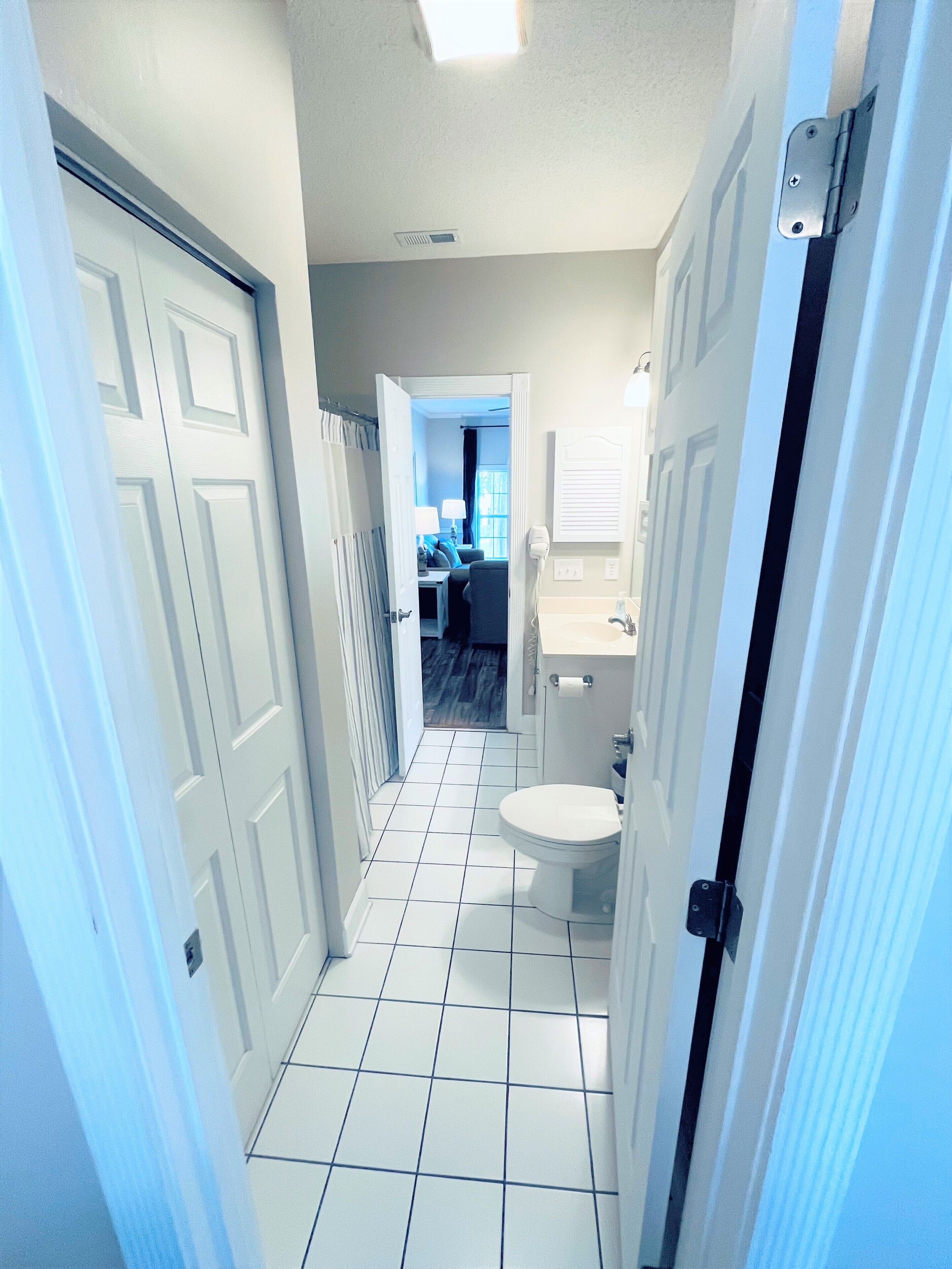A narrow hallway with white tiled floors leading to a bathroom with a toilet and sink.