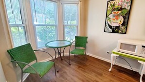 Ein Zimmer mit einem runden Tisch und zwei grünen Stühlen, einer weißen Mikrowelle auf einem kleinen Tisch und einem Bild an der Wand.