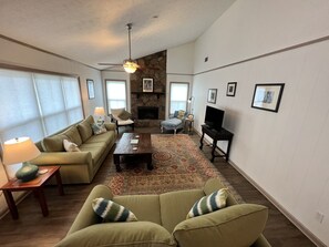 A living room with a sofa, armchairs, a coffee table, a fireplace, a television, and a ceiling fan.