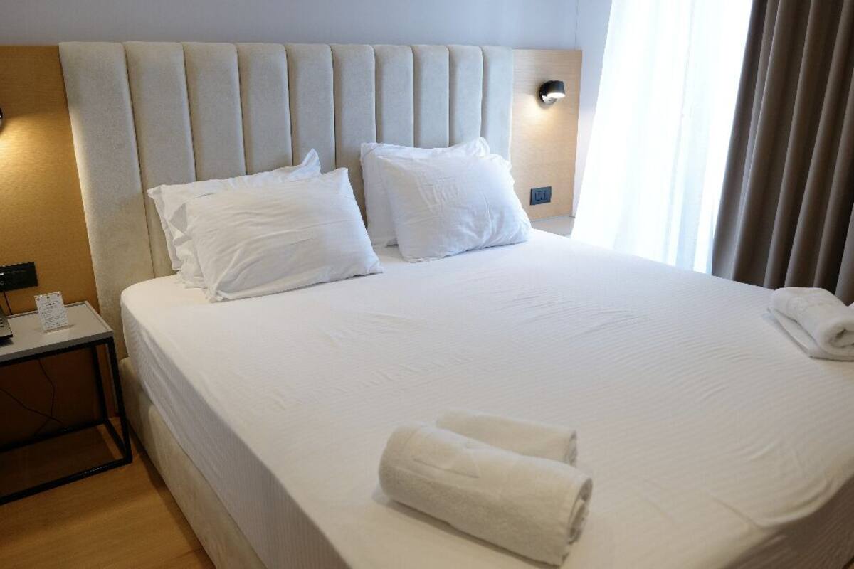 A hotel room with a large bed, two pillows, a nightstand with a phone, and a window with curtains.