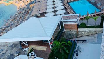 A rooftop pool area with multiple lounge chairs and umbrellas, a swimming pool, and a view of the beach and ocean.