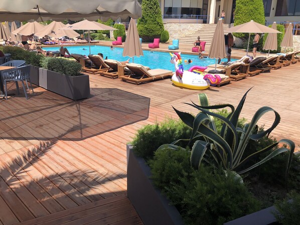 A pool area with lounge chairs and umbrellas, surrounded by greenery and a wooden deck. - Andon Lapa Suites (Sarandë)
