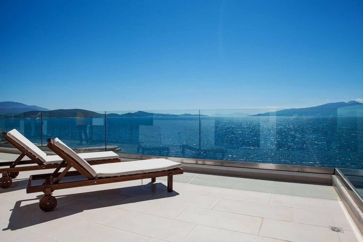 A balcony with two sun loungers overlooking a body of water and distant mountains.