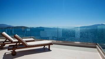 A balcony with two sun loungers overlooking a body of water and distant mountains.