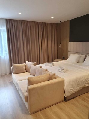 A modern hotel room with a large bed, two sofas, and a large window with curtains. - Andon Lapa Suites (Sarandë)
