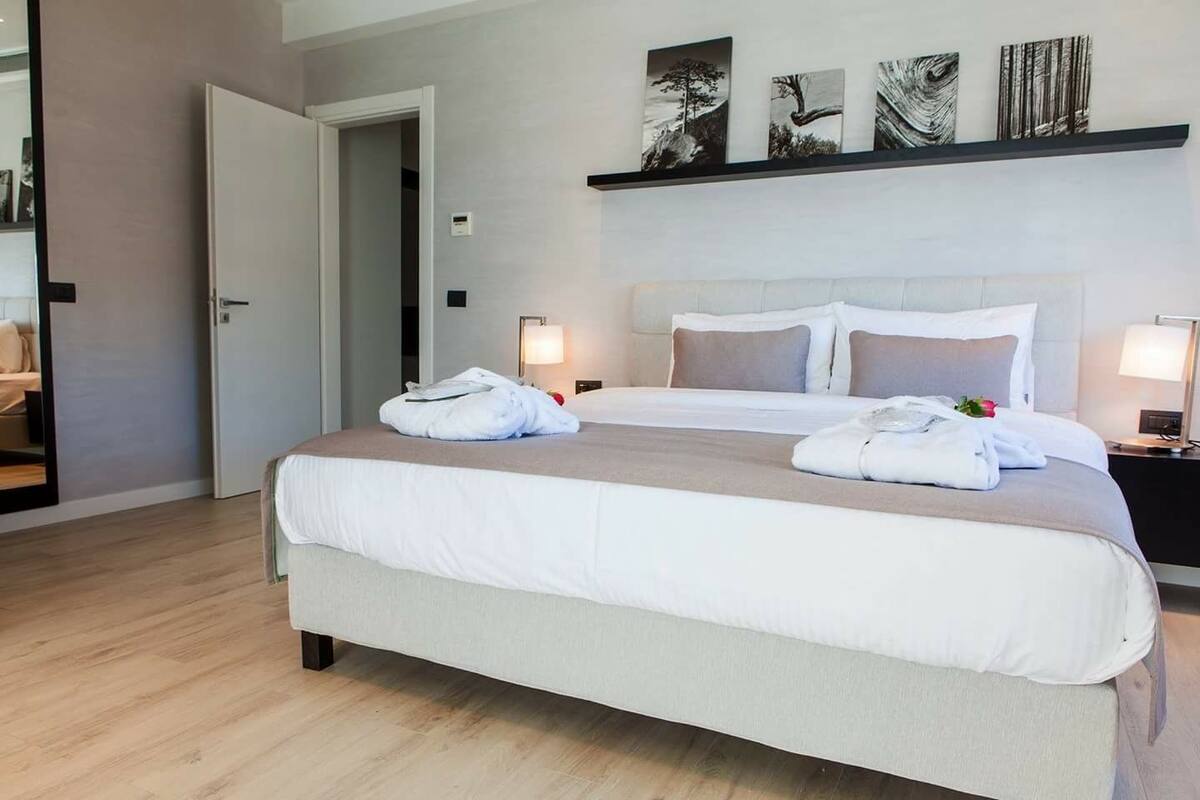 A neatly made bed with white linens, two bedside tables with lamps, and a door leading to another room.