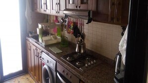 Cuina amb armaris de fusta, fogó, rentadora i cafetera.