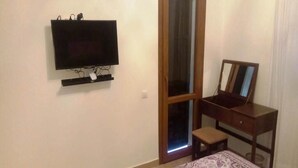 Un dormitori amb llit, televisió penjada a la paret, escriptori de fusta amb mirall i una porta corredissa de vidre.