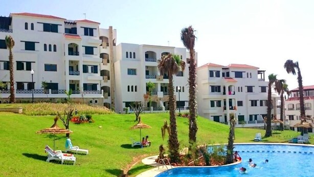 Piscina envoltada d'una zona verda amb gandules i palmeres.