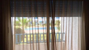 A window with sheer curtains, a view of a pool, and a blue fence.