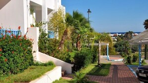 A white building with blue balconies, surrounded by lush greenery and a clear blue sky.