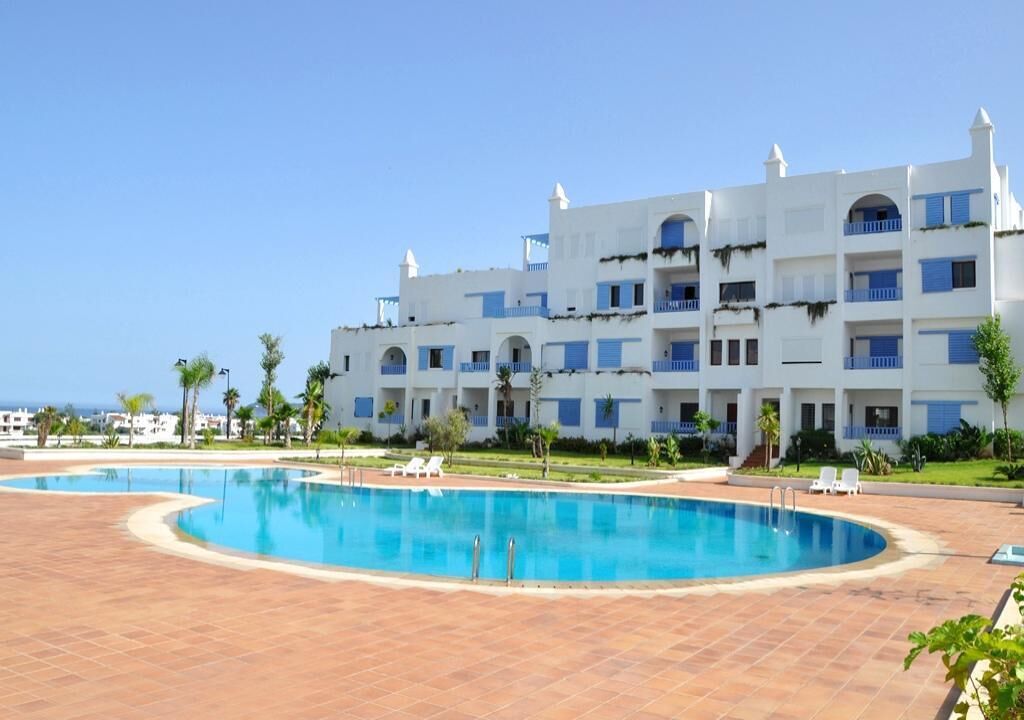 A hotel with a large swimming pool, multiple balconies, and a view of the sea.