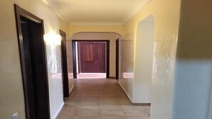 A hallway with a tiled floor, a wooden door, and a light fixture on the wall.