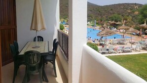 Ein Balkon mit Tisch und Stühlen, der einen Poolbereich mit Sonnenschirmen und Liegestühlen überblickt.