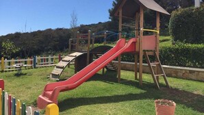 Ein Spielplatz mit einer roten Rutsche, Klettergerüsten und einer Holzüberdachung.