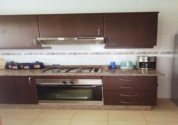 A kitchen with dark brown cabinets, a gas stove, an oven, and a coffee maker.