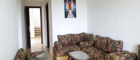 Una sala de estar con sofá, una mesa de centro y televisor. Hay un cuadro en la pared y una puerta que da a otra habitación.