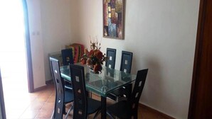Ein Essbereich mit einem Glastisch und schwarzen Stühlen, einer Vase mit Blumen und einem farbenfrohen, abstrakten Gemälde an der Wand.