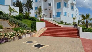 A multi-story hotel with a red staircase leading to the entrance, surrounded by landscaped gardens and palm trees. - Residence Smir Park Beach 1672 (Mdiq)
