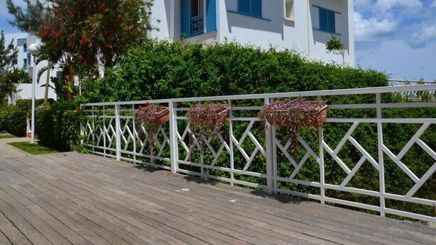 A white building with blue shutters and balconies, a wooden deck, and a white fence with hanging flower pots. - Residence Smir Park Beach 1672 (Mdiq)