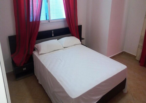 A single bed with white bedding, a black headboard, and red curtains.