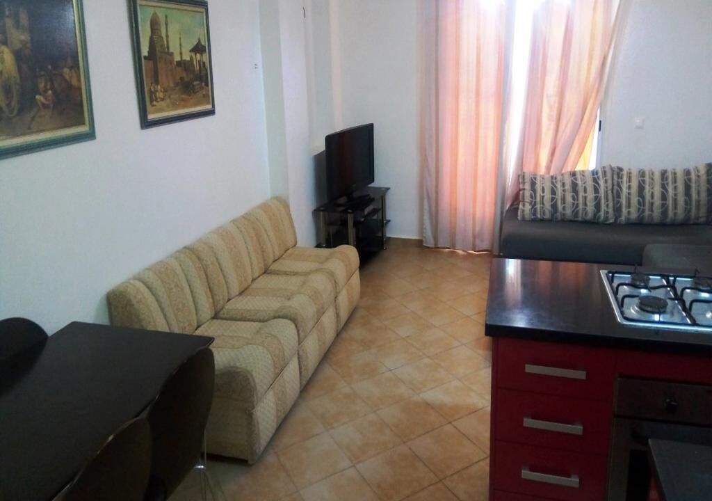 A living room with a sofa, a TV, and a kitchen area with a stove.