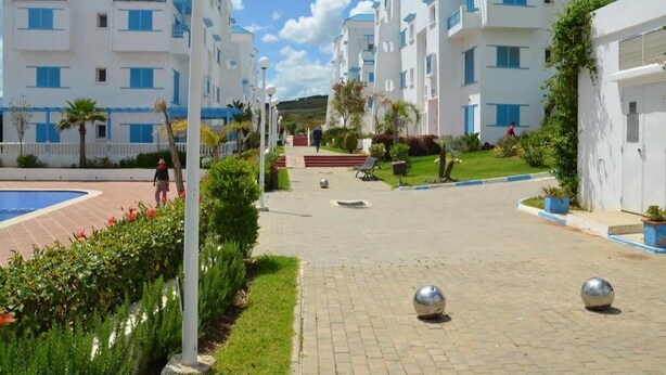 Une cour intérieure agrémentée de bâtiments modernes aux façades blanches, d’une piscine et d’un chemin pavé.