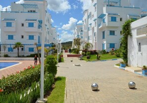 A courtyard with modern white buildings, a swimming pool, and a paved walkway. - Smir Park Beach Residence 4537 (Mdiq)