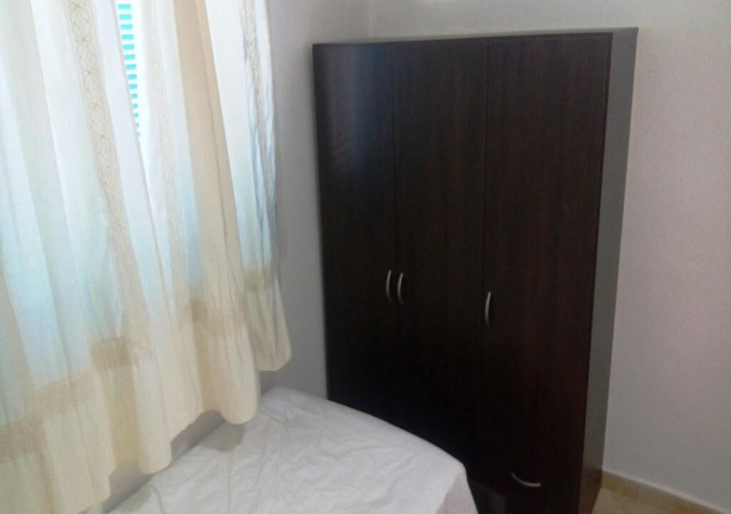 A room with a bed, a dark wooden wardrobe, and sheer curtains.