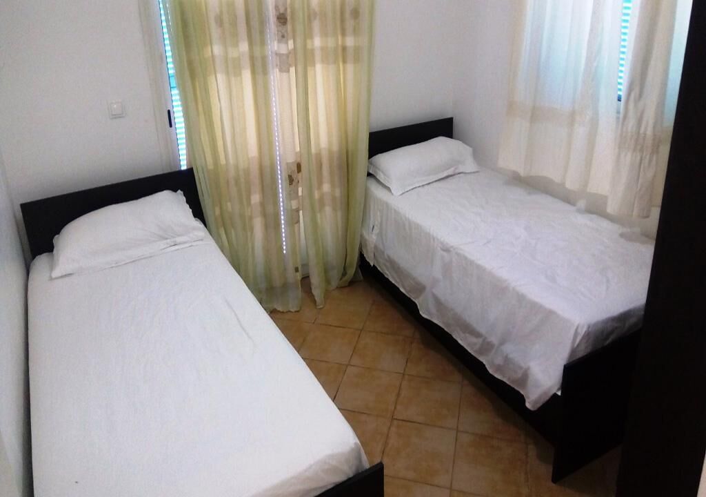 A room with two single beds, a window with blinds, and a curtain.