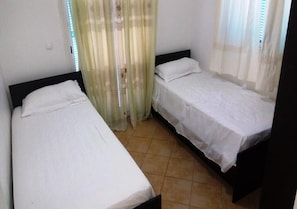 Quarto com duas camas individuais, janela com persianas e cortina.