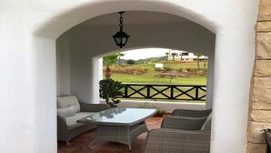 Un patio cubierto con mobiliario de mimbre, una mesa de vidrio y vistas a un campo de golf.
