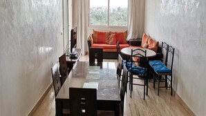 A dining area with a long table and chairs, a sofa with orange cushions, and a view of greenery through a window. - Residence Playa Del Pacha 4858 (Mdiq)