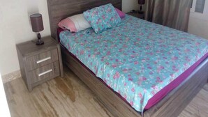 A bedroom with a wooden bed, floral bedspread, two bedside tables, and a nightstand with drawers. - Residence Playa Del Pacha 1914 (Mdiq)