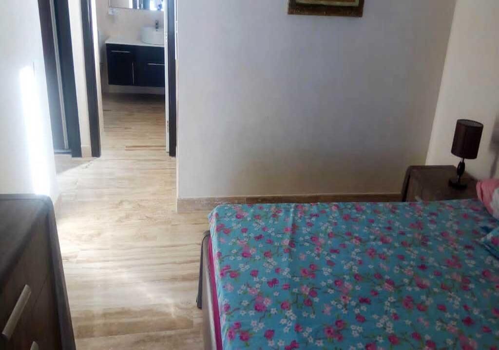 Un dormitorio con cama, mesita de noche y lámpara. Hay una puerta que da al baño.