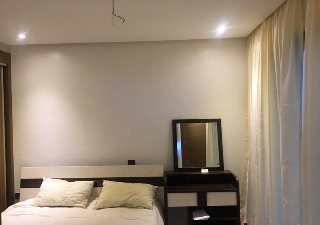Een hotelkamer met een bed, een nachtkastje met spiegel en een raam met gordijnen.